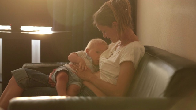 年轻的母亲，在日落时分，在宁静的傍晚，在阳光明媚的客厅里喂她的小男孩视频素材