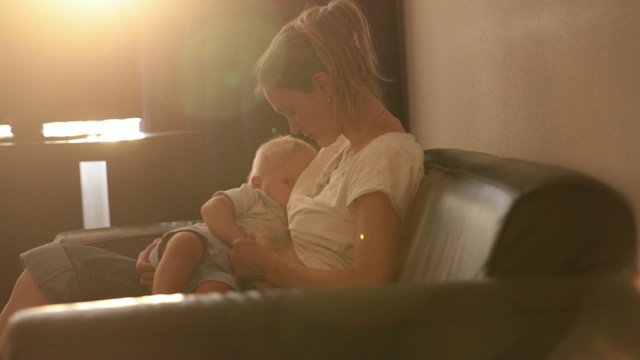 年轻的母亲，在日落时分，在宁静的傍晚，在阳光明媚的客厅里喂她的小男孩视频素材