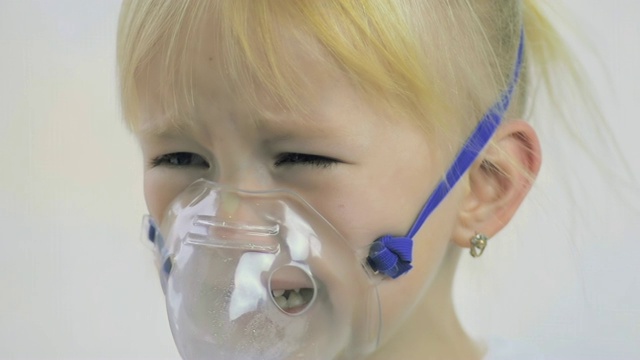 一个四岁女孩通过一个吸入器面具在医院做呼吸程序的特写。视频下载