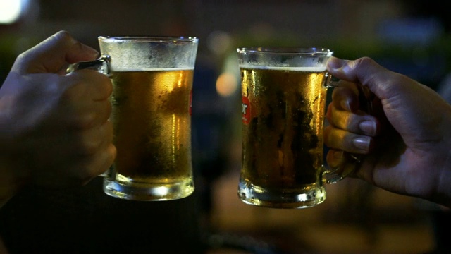 慢动作FHD镜头的两个亚洲人祝酒和碰杯啤酒，一起在酒吧和餐厅欢呼，放松和饮料的概念视频下载
