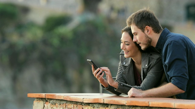 一对兴奋的情侣在阳台上查看手机内容视频素材