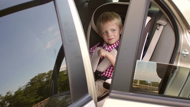 一个5岁的穿着红衬衫的快乐男孩坐在汽车座椅上玩耍。视频素材