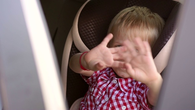 一个愉快的婴儿坐在儿童座椅上挥手致意。视频素材