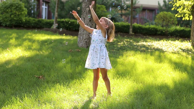 一个可爱的小女孩穿着夏装在公园里玩肥皂泡视频素材