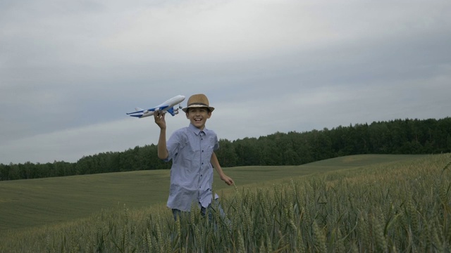戴着草帽的快乐男孩梦想家手里拿着一架飞机跑过田野视频素材
