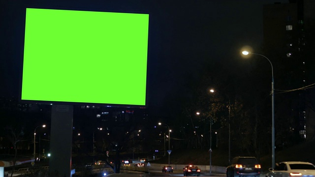 有绿色屏幕的广告牌，位于繁忙的街道上。汽车在晚上行驶。视频素材