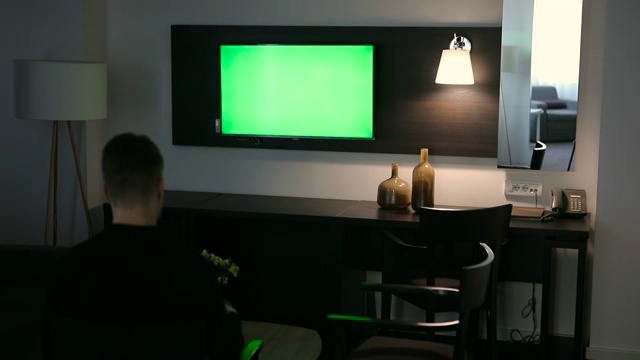 一个男人正在酒店房间里看绿屏电视视频素材
