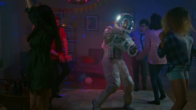 在大学宿舍的化妆舞会上:有趣的家伙穿着太空服跳舞，跳着时髦的机器人现代舞。和他在一起漂亮的女孩和男孩在霓虹灯下跳舞。在缓慢的运动。视频素材