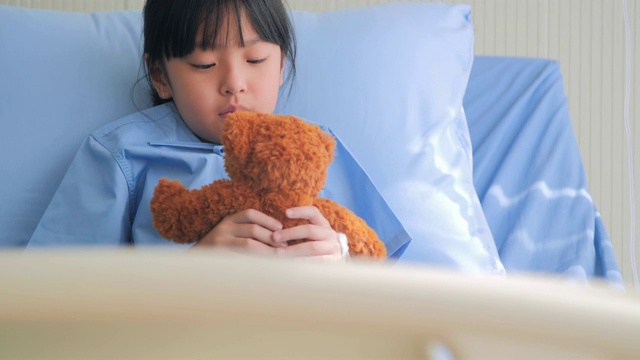 女婴在医院里喜怒哀愁的坐在床上，独自看着泰迪熊。紧张的时刻视频素材