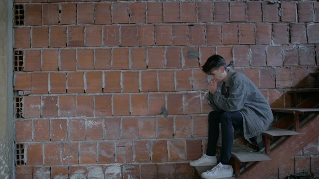 悲伤的少年坐在砖墙旁视频素材