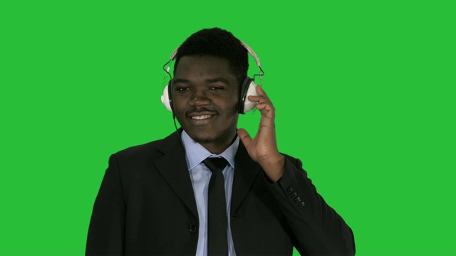 英俊的非洲裔美国商人戴着耳机在绿色屏幕上听音乐，Chroma Key视频素材