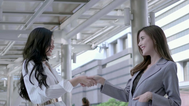 在泰国市中心，两位女商人谈论新的创业项目，握手成交，愉快地微笑着。协议，会议，商业成功概念。慢动作视频素材