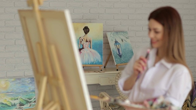一个穿着白衬衫的年轻性感的女孩在画室的画布上画画。艺术视频素材