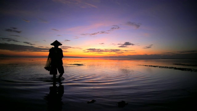 日落剪影巴厘岛男性在印尼海滩钓鱼视频下载