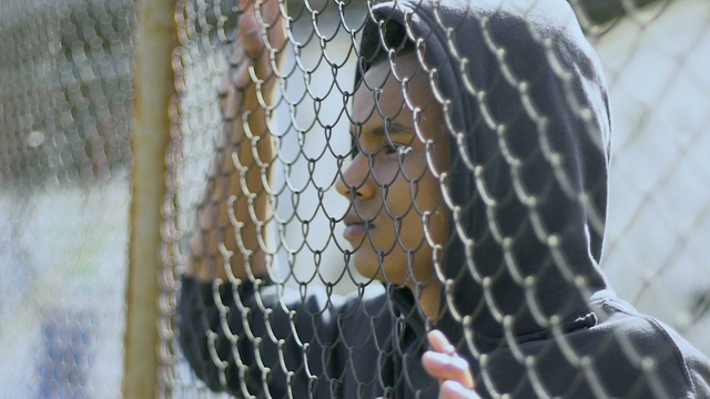 混血男孩站在铁栅栏附近，觉得自己和社会之间有障碍视频素材