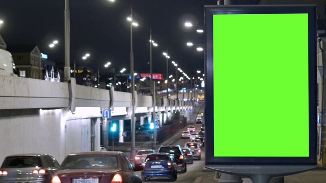 有绿色屏幕的广告牌，位于繁忙的街道上。汽车在晚上行驶。视频素材