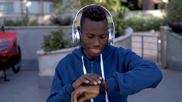 年轻的非洲男孩戴着耳机，从智能手表上开始播放音乐视频下载