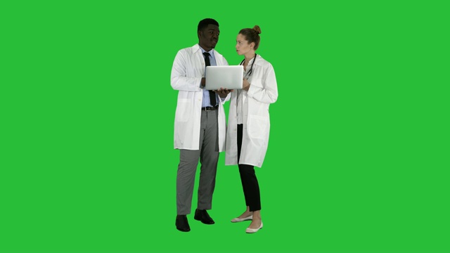 医务人员在一台灰色笔记本电脑前工作，同时站在绿色屏幕上视频素材