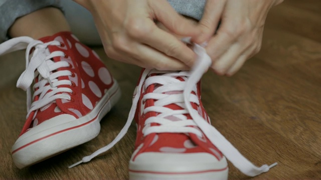 一个女人坐在地板上系着红色运动鞋的鞋带。特写女孩的手系鞋带准备运动，走在街上。视频素材