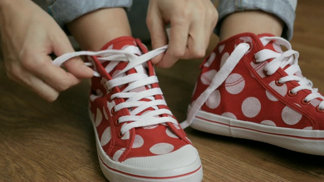 一个女人坐在地板上系着红色运动鞋的鞋带。特写女孩的手系鞋带准备运动，走在街上。视频下载