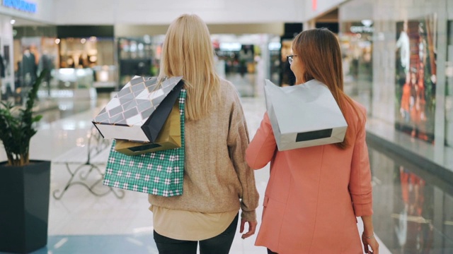 慢镜头，快乐的年轻女性朋友一起走在购物中心，拿着明亮的袋子，然后转向镜头和微笑。购物狂和商店的概念。视频素材