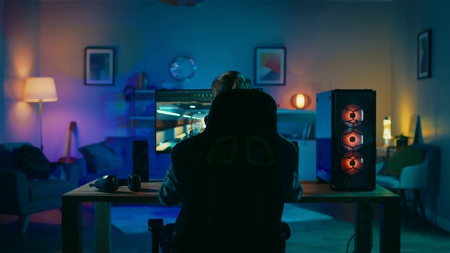 Back Shot of a Gamer Playing and Winning in First-Person Shooter Online Video Game on His Powerful Personal Computer.一个玩家在他的强大的个人电脑上玩第一人称射击在线视频游戏并获胜。房间和电脑都有彩色霓虹灯。温馨的家庭之夜。视频素材