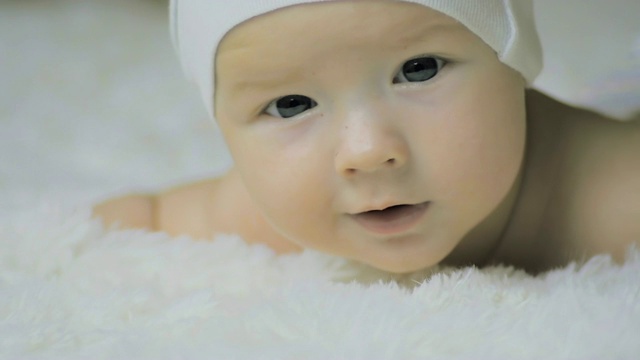 一个6个月大的婴儿戴着头饰，躺在婴儿床上的白毯子上。视频下载