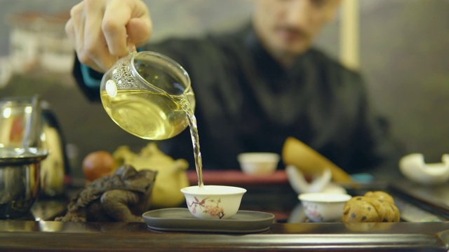 师傅将绿茶从玻璃茶壶中倒进白杯子里视频素材