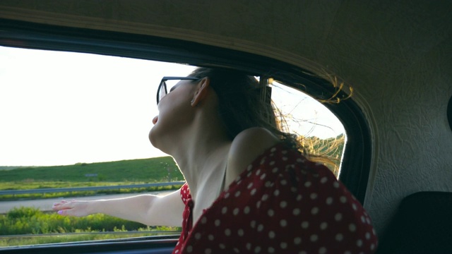年轻迷人的女孩倚在车窗外老爷车和享受在夏天的时间。旅行和自由的概念。夏天阳光灿烂的日子。内景慢动作特写视频素材
