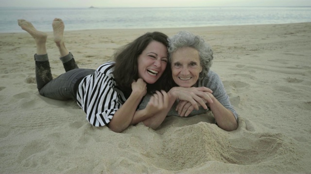 快乐的成年女人躺在沙滩上玩视频下载
