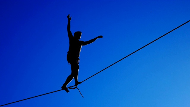 绳子。在蓝天的背景下，一个人在绳子上行走的剪影。视频下载
