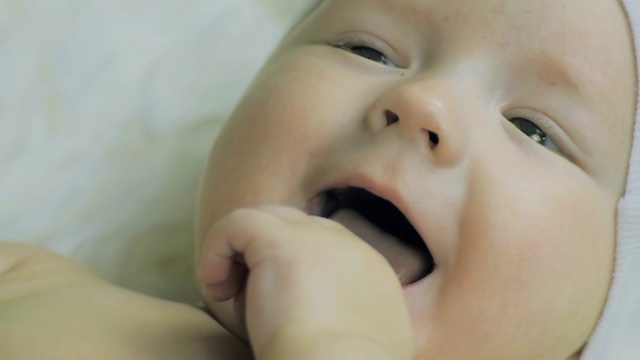 一个6个月大的男孩戴着头饰，躺在白毯子上，面带微笑。视频素材