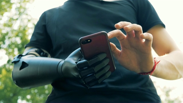 一名年轻人戴着假手使用智能手机。未来的概念。视频下载