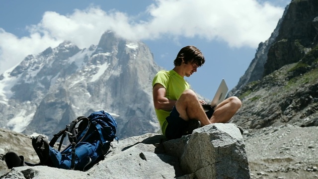 男游客自由职业者远程工作的自然和使用电脑在山上坐在一块石头上的特写，慢动作视频下载