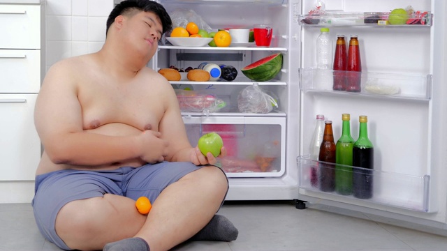 超重的男人打开冰箱，吃了一顿很晚的晚餐，然后坐在冰箱前睡觉。真实的身体视频下载