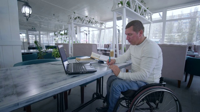 残疾学生坐在轮椅上用笔记本电脑进行视频教育，从网上教学中学习，在笔记本上做笔记视频下载