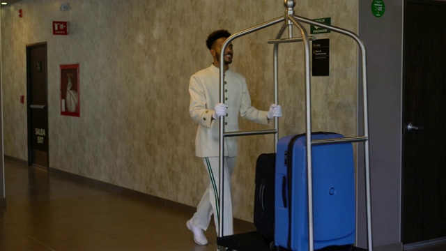 友善的行李员推着行李车穿过酒店走廊，面带微笑视频下载