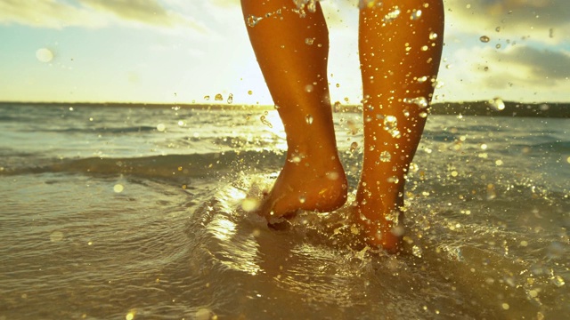 镜头光晕:日落时分，一个不认识的赤脚女孩沿着热带海岸行走。视频素材