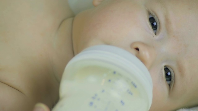 一个六个月大的男孩躺在床上吃奶瓶里的牛奶。视频下载