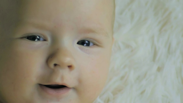 一个六个月大的男孩躺在白色的婴儿床上微笑着看着慢镜头。视频下载