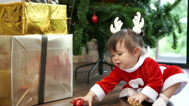 可爱的1岁小女孩戴着驯鹿头带玩圣诞装饰品和圣诞树的背景。圣诞快乐，节日快乐!视频购买