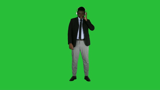 英俊的非洲裔美国商人戴着耳机在绿色屏幕上听音乐，Chroma Key视频素材