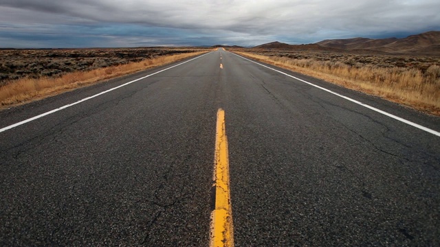 低角度POV空铺沥青公路与虚线通过熔岩和山艾树沙漠景观。视频下载