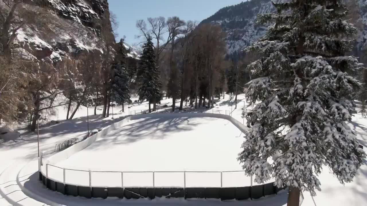 上升无人机拍摄的一个小户外冰雪覆盖的溜冰场被雪松包围在一个明亮的冬天的一天视频素材