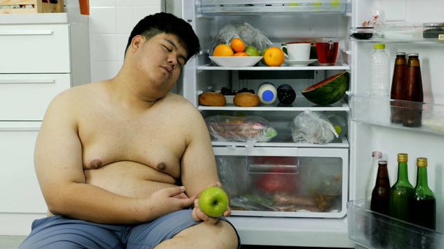 胖男人坐在冰箱旁边睡觉。视频下载
