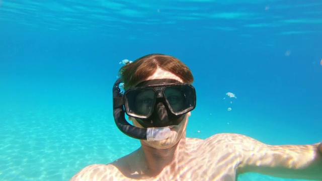 图为克罗地亚佩列沙茨，一名顽皮的男子在阳光明媚的蓝色海洋中戴着可穿戴的相机浮潜视频素材