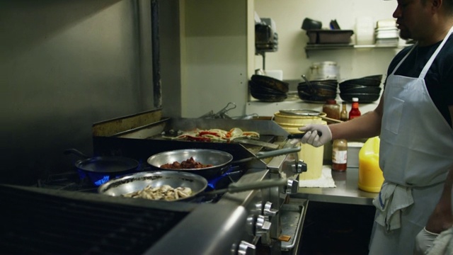 西班牙裔厨师(十几岁和三十岁)在墨西哥餐厅的炉子和煎锅上为法士达准备蔬菜、肉和蘑菇视频素材