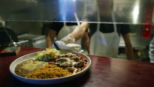 在一家墨西哥餐厅，一名厨师将一盘热的墨西哥食物递到服务员的服务窗口视频素材