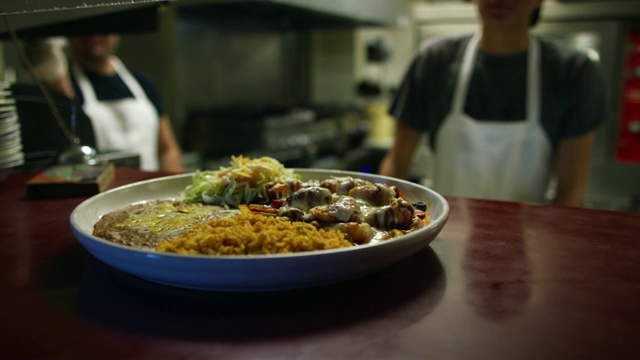 在一家餐馆里，一位十几岁的墨西哥男厨师把一盘从厨房里拿出来的热墨西哥菜从窗户里递了过去，然后摇了摇铃视频素材