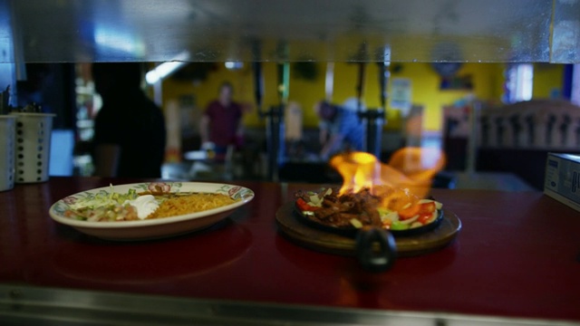 一名女服务员走进一家墨西哥餐厅，厨师在服务窗口点上一盘法士达(火焰)视频素材